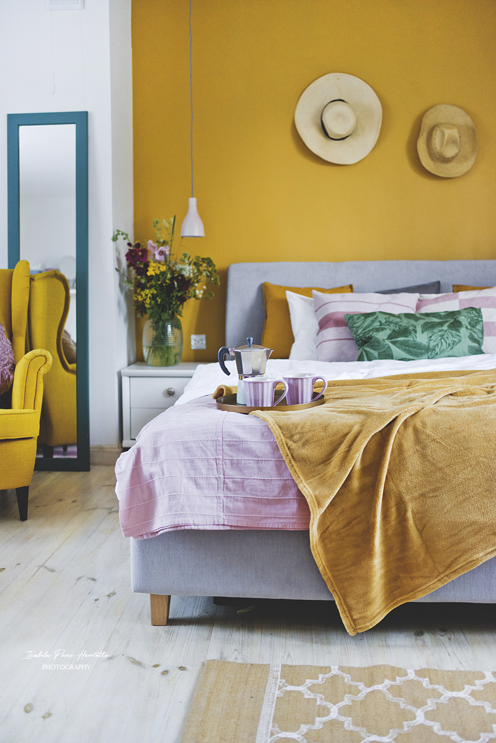 sypialnia, miodowa ściana, tapicerowane łóżko, bukiet polnych kwiatów, lampki nocne, kapelusze na ścianie,kolorowe wnętrze